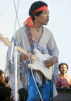 a man with an electric guitar in front of a microphone and some other people behind him