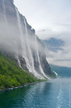 the water is crystal blue and green as it pours from the side of a mountain