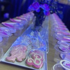 decorated cookies and cupcakes sit on a long table with plastic wrappers around them