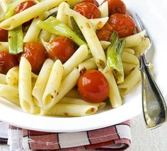 a white bowl filled with pasta, tomatoes and celery next to a fork