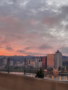 the city skyline is lit up at sunset with clouds in the sky and water below