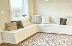 a white bench with pillows on top of it in front of a window and rug