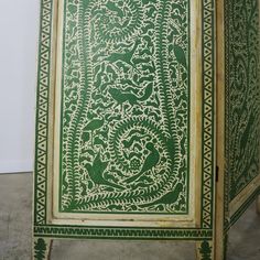 a green and white table with intricate designs on the top, sitting in front of a wall