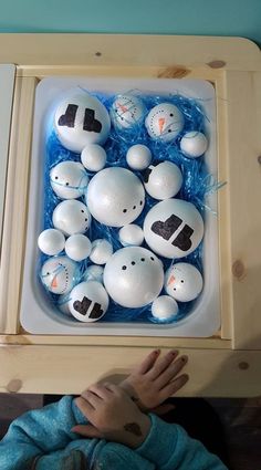 a child is sitting in front of an open box filled with plastic snowman balls