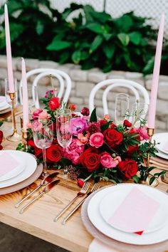 the table is set with pink and red flowers, candles, and place settings for dinner