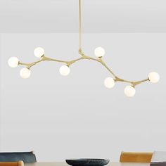 a modern chandelier hangs over a dining room table with chairs and a bowl on it