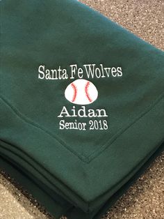 a green sweatshirt with a baseball embroidered on the front and back, sitting on top of a carpeted floor