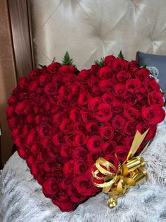 a heart - shaped arrangement of red roses on a bed with a gold ribbon and bow