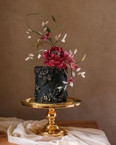 a black and gold cake with red flowers on the top is sitting on a table