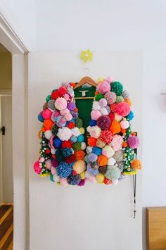 a colorful jacket hanging on a wall with pom - poms all over it