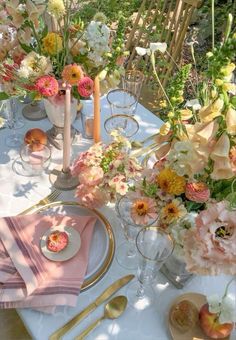 the table is set with pink and yellow flowers in vases, plates, napkins and silverware