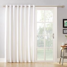 a white curtain hanging on the side of a window next to a table and chair