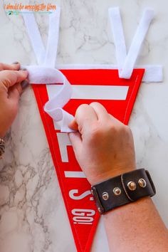 someone cutting out the letters on a red pennant with white tape and scissors to make it look like they have been made from construction paper