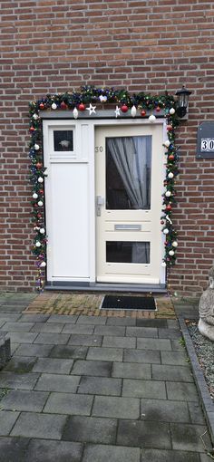 a white door with christmas decorations on the side of it and a brick wall behind it