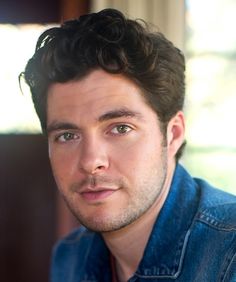 a close up of a person wearing a denim shirt and looking at the camera with a serious look on his face