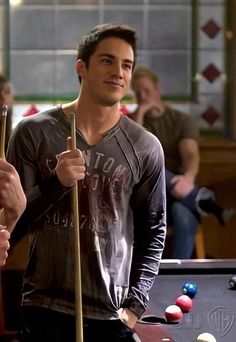 a man standing next to a pool table holding a cue in one hand and a ball in the other