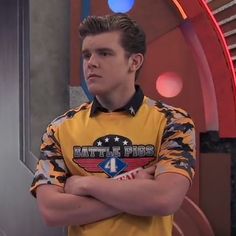 a young man in a yellow shirt is standing with his arms crossed