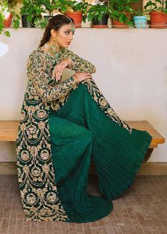 a woman sitting on top of a wooden bench wearing a green and gold dress with long sleeves