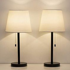 two lamps sitting next to each other on top of a white tablecloth covered floor