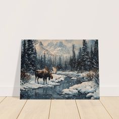 a moose standing in the snow next to a river and mountains with pine trees on it