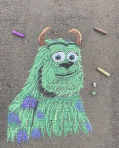 a crayon drawing of a green monster with long horns and blue feathers on the ground next to colored crayons