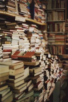 many books are stacked on top of each other in a room full of bookshelves