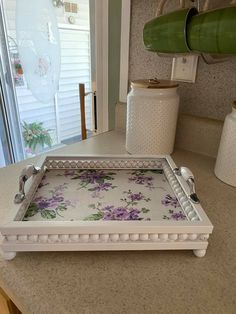 a white tray with purple flowers on it sitting on a kitchen counter next to a window