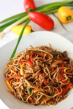 a white bowl filled with noodles and vegetables on top of a table next to peppers