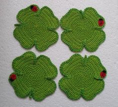 four green crocheted coasters with ladybugs on them sitting on a white surface