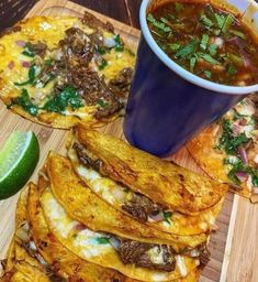 a wooden cutting board topped with lots of food next to a bowl of soup and a slice of lime