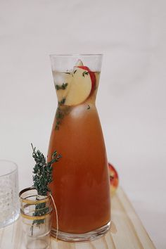 a glass pitcher filled with liquid sitting on top of a wooden table next to an apple slice