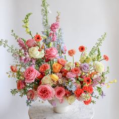 a white vase filled with lots of colorful flowers on top of a marble topped table