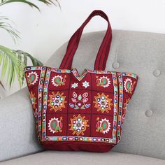 Featuring the traditional Kutch embroidery that is typical on Gujarat textiles, this shoulder bag is a standout. The bag is presented by SEWA, a non-profit that works to promote employment opportunities for women in India. Crafted from burgundy cotton, the shoulder bag is lavishly embellished with colorful embroidery and tiny mirrors. The fully lined tote features convenient interior pockets and a magnetic snap closure. Traditional Red Embroidered Shoulder Bag, Red Embroidered Bag, Red Handwork Shoulder Bag For Festivals, Red Shoulder Bag With Handwork For Festivals, Festival Red Shoulder Bag With Handwork, Embroidered Rectangular Bags For Festivals, Red Handwork Bag For Everyday Use, Traditional Multicolor Embroidered Bag For Daily Use, Traditional Rectangular Bags With Multicolor Embroidery