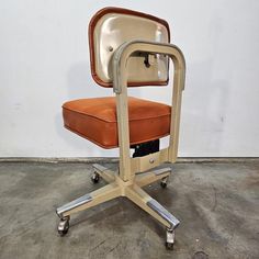 an orange chair sitting on top of a metal frame with wheels and casteors in front of a white wall