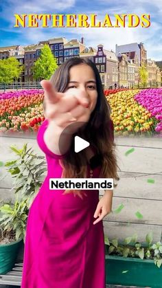 a woman in a pink dress is pointing her finger at the camera with flowers behind her