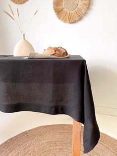 a table topped with a loaf of bread next to a white vase and wall hangings