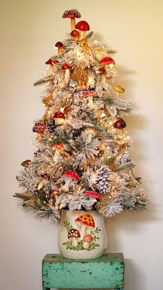 a white christmas tree with mushrooms and other decorations on it's top, sitting in front of a wall