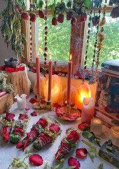 a table topped with candles and flowers next to a window filled with greenery on top of a white cloth covered table