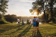 a group of people standing on top of a lush green field next to a lake