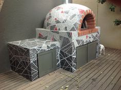 an outdoor pizza oven sitting on top of a wooden deck next to a wall and potted plant