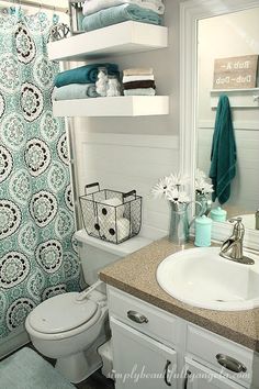 a bathroom with blue and white decor on the shower curtain, shelves above the toilet