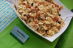 a dish of pasta with olives and peppers on a green table cloth next to a fork