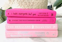 three pink books stacked on top of each other in front of a white pillow and plant