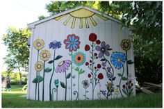 a painted outhouse in the grass with flowers and sunbursts on it