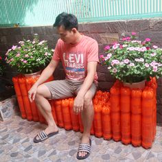 a man sitting on top of orange plastic barrels filled with flowers