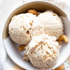 two scoops of ice cream in a bowl on a white tablecloth with nuts