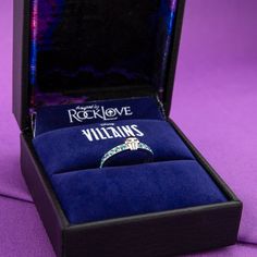 a ring in a velvet box sitting on a purple cloth