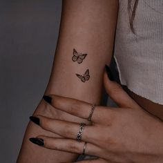 two women with matching rings and butterfly tattoos on their arms, both holding each other's hands