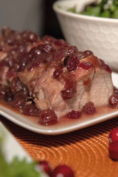 a white plate topped with meat covered in cranberries next to a bowl of salad