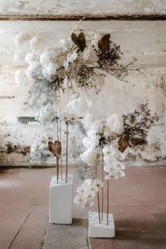 three white vases with flowers in them sitting on a cement floor next to a brick wall